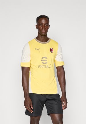 Maglia da calcio gialla e avorio con maniche corte, logo Puma, testo "eFootball" in grigio e emblema dell'AC Milan. Indossata con pantaloni corti neri.
