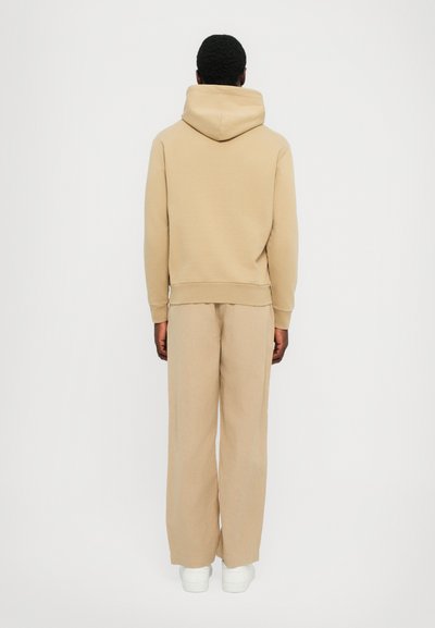 Beige hoodie med en rymlig huva och ribbade ärmslut, i kombination med löst sittande beiga byxor. Plaggen har en mjuk tygkvalitet och en minimalistisk design.