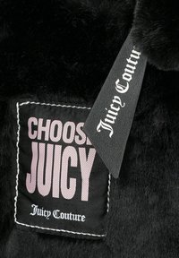 Zwart nepbont materiaal met een rechthoekig label waarop "KIES JUICY" in het roze staat en "Juicy Couture" in witte tekst. Het label is zwart.