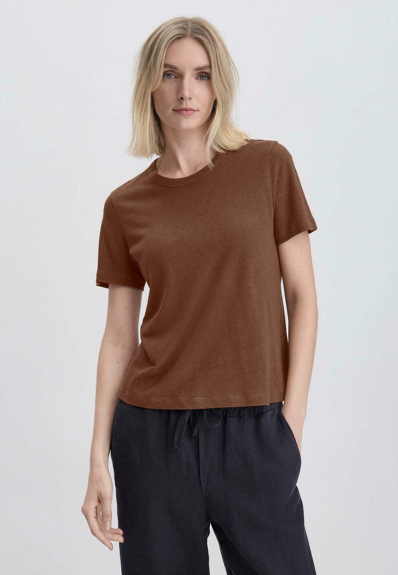 T-shirt corto marrone a maniche corte realizzato in tessuto morbido, caratterizzato da scollo rotondo, vestibilità ampia e dettagli di cucitura minimi. Indossato con pantaloni scuri.