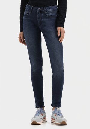 Dark blue skinny jeans made of denim, featuring a classic five-pocket design and subtle fading. Paired with gray and orange athletic shoes.