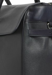 Schwarze Lederhandtasche mit genarbter Textur, einem glatten oberen Klappdeckel und einem Akzent aus Metallbeschlägen. Seitenansicht zeigt ein strukturiertes Design.