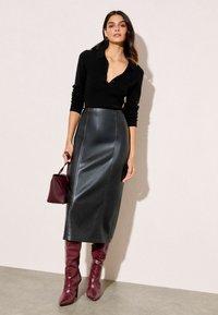 Melnā adīta džemperis ar apkakli, kombinēts ar melnu augsto vidukli ādas svārku. Aksesuāri ietver bordo rokassomu un spīdīgas līdz ceļiem zābaki.