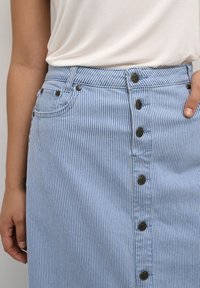 Denim krilo s črtami v modri in beli barvi, ki ima oprijet pas, zapiranje na gumb in dve sprednji žep. Teksturiiran material in kontrastni črni gumbi.