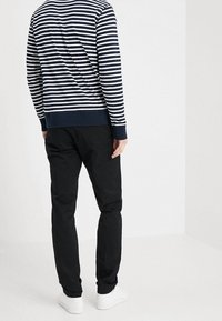 Felpa a righe blu navy e bianca con polsini e orlo a coste, abbinata a pantaloni neri e sneaker bianche. Vista dal retro.
