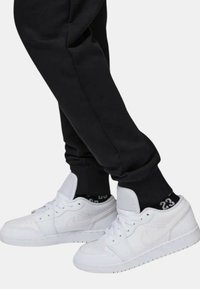 Sneaker Nike bianche con tomaia in pelle liscia, design low-top e punta perforata. Joggers neri con polsini a costine parzialmente visibili.