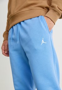 Lichtblauwe joggingsbroek met een gladde textuur, voorzien van een wit Jordan-logo op de linker bovenbeen en een elastische tailleband met trekkoorden.
