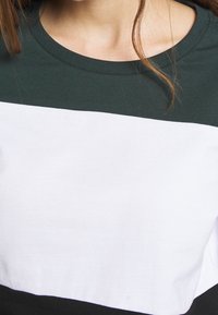 Kortärmad topp med en färgblockdesign i mörkgrön, vit och svart. Tillverkad av mjuk bomull med en ribbad krage.