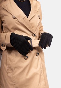 Beige trench coat with double-breasted buttons and a belted waist; paired with black gloves featuring a ribbed texture and finger detailing.