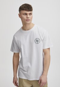Hvid bomulds T-shirt med korte ærmer, rund halsudskæring og sort grafiktryk på venstre bryst med en stiliseret rose og tekst.