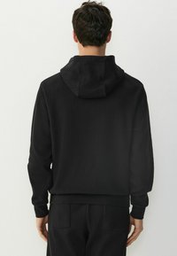 Hanorac negru cu un design texturat, în dungi. Dispune de o glugă cu șnur, manșete și tiv cu nervuri. Este asortat cu pantaloni coordonați.