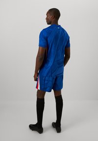 Sportshirt en short set in levendig blauw, met een gestructureerd ontwerp. Inclusief zwarte sokken en zwarte voetbalschoenen; opmerkelijke stofdetails aanwezig.