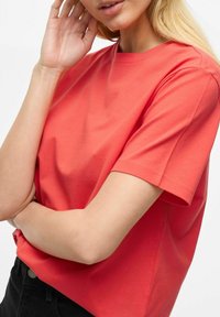 Koralfarvet kortærmet t-shirt lavet af blødt bomuld med rund halsudskæring og afslappet pasform, der har en glat overflade og minimal syning.