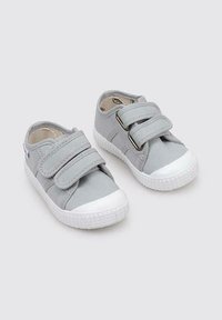 Baskets en toile grises avec semelles en caoutchouc blanches, dotées de deux bandes Velcro et d'une semelle texturée à motifs pour une meilleure adhérence.