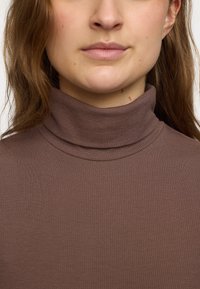 Hnedý rebrovaný rolák s priliehajúcim strihom a textúrovanou látkou, s vysokým golierom a jemnými švovými detailmi.