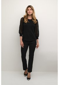 Haut noir avec dentelle, manches bouffantes trois-quarts ; associé à un pantalon noir ajusté et des talons ouverts noirs. Design simple et élégant.