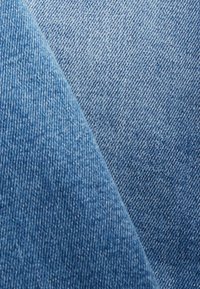 Tela de mezclilla en tonos azul claro con un tejido texturizado, que muestra líneas diagonales de sarga y ligeras variaciones en color.