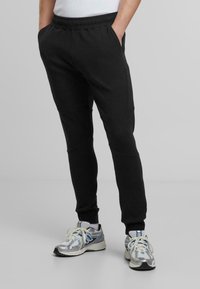 Svarta joggarbyxor gjorda av ett mjukt, stretchigt material, med elastisk midja, sidofickor och avsmalnande muddar.