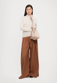 Beige høyhalset genser, brede brune plisserte bukser og en myk beige håndveske. Glatte teksturer med et minimalistisk design.