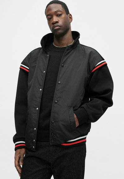 Must mustreppjakker, mille on kapuuts, nööpide ja soonikkudega varrukad, samuti kontrastsed punased, valged ja sinised triibud õlgadel.