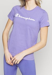 Lila bomull t-shirt med en vit "Champion" logga över bröstet, kortärmad och med en klassisk rund hals.
