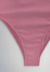 Mauve ribbed fabric close-up of high-cut, seamless underwear or swimsuit bottom with double-stitched seams on gray background.