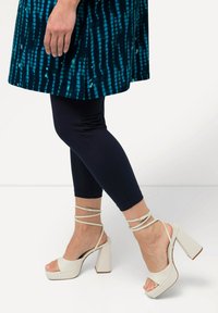 Sandales blanches à talons hauts avec un large talon bloc et des brides de cheville, assorties à des leggings navy et à une robe turquoise à motifs.