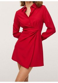Robe chemise rouge à manches longues avec un col. Dotée d'une fermeture à boutons et de détails drapés sur le côté, fabriquée en tissu lisse.