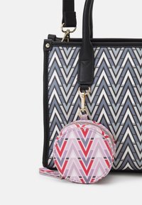 Sac fourre-tout à motifs zigzag gris et noir avec des anses noires ; doté d'une pochette ronde à motifs rose, rouge et blanc attachée par un fermoir en or.