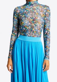 Blommönstrad, genomskinlig topp med långa ärmar och hög halsringning, kombinerad med en flytande blå plisserad kjol med en smockad midja.