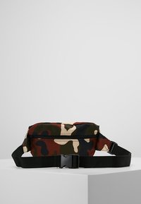 Marsupio mimetico con cintura nera regolabile, chiusura con zip e una combinazione di motivi verdi, marroni e crema su tessuto resistente.