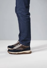 Heren sneakers met een mix van marineblauw suède en grijs mesh, voorzien van een dikke bruine zool en contrasterende veters voor extra detail.