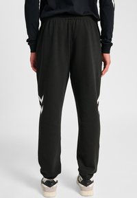 Zwarte sweatpants met een elastische tailleband, met witte grafische accenten aan de zijkanten. De stof lijkt zacht en textuur te hebben.