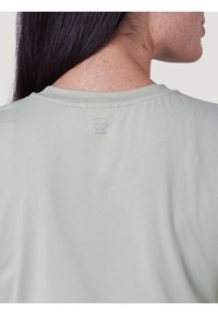 Maglietta verde chiaro a maniche corte con una texture liscia, caratterizzata da un collo rotondo e un logo discreto stampato sulla parte posteriore.