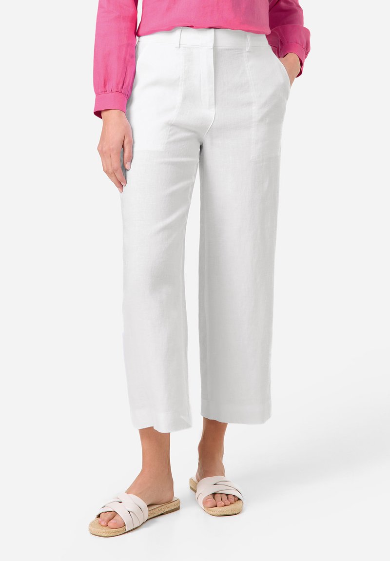 Weisse Leinen-Hosen mit weitem Bein und Fronttaschen, ausgestattet mit einem klaren Schnitt und einer subtilen Textur, kombiniert mit hellen flachen Sandalen.