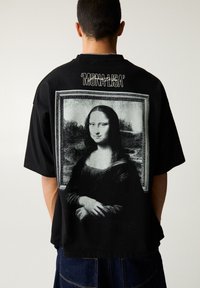 Schwarzes T-Shirt mit einem großen, einfarbigen Druck der Mona Lisa auf der Rückseite, mit dem Text 'MONA LISA' über dem Bild.