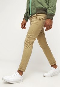 Khaki chinos z bavlny, slim fit design, délka do kotníků, se pěti kapsami, doplněné bílými teniskami a zelenou bomber bundou.