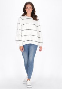 Maglione bianco a maglia con strisce orizzontali nere, scollatura rotonda e maniche ampia, abbinato a jeans skinny azzurri chiari e sneakers bianche.