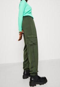 Zielone spodnie cargo wykonane z miękkiego materiału, z elastycznymi mankietami, kieszeniami po bokach i luźnym krojem, w zestawieniu z jasnoniebieską bluzką z długim rękawem.