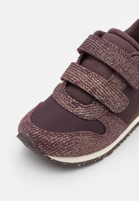 Scarpa sportiva viola con una superficie testurizzata e scintillante. Presenta due cinturini in Velcro e una soletta imbottita, progettata per il comfort.