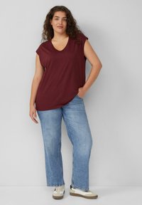 Bordeaux v-hals top met korte mouwen, losse pasvorm, gecombineerd met lichtblauwe wijde jeans en beige sneakers met witte accenten.