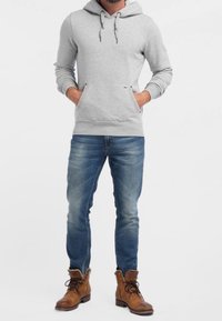 Grauer Hoodie mit einer Kängurutasche und verstellbarem Kapuzenzug, kombiniert mit blauen Jeans und braunen Schnürstiefeln. Lässige, entspannte Passform.
