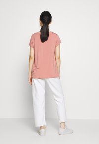 T-shirt a maniche corte, dalla vestibilità rilassata, in rosa polveroso, abbinato a pantaloni bianchi a gamba larga. La maglietta ha una texture liscia e un colletto rotondo.