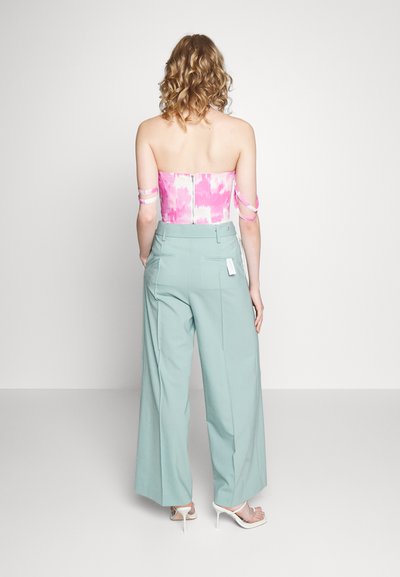 Top sem alças em padrão tie-dye rosa, com fitas laterais, combinado com calças largas de cintura alta em verde menta e sandálias de salto transparente.