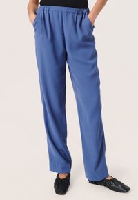 Blå, löst sittande byxor med elastisk midja och sidofickor. Tillverkade av mjukt tyg, med rak benpassform och en enfärgad nyans.