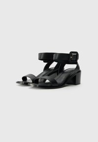 Svarte lær blokkhæl sandaler med to brede stropper over tåa og en spenneankelstropp. Glatt tekstur og minimalistisk design.