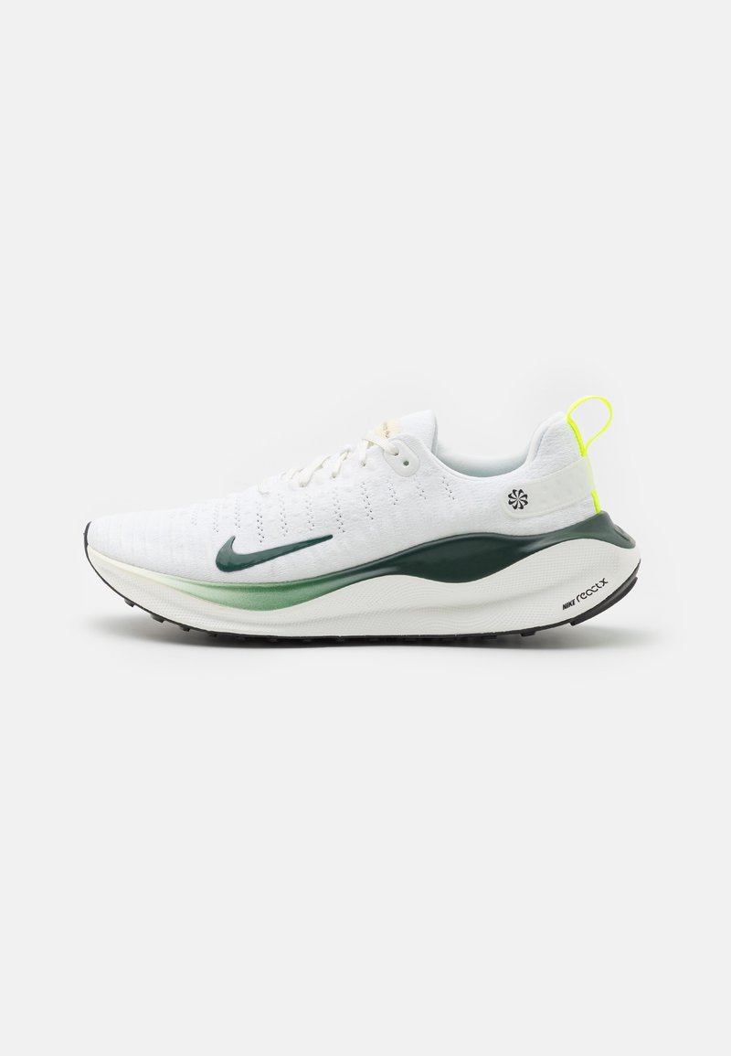 Chaussure de sport blanche avec logo Swoosh vert, semelle épaisse verte et blanche, et languette jaune au talon, vue de côté sur un fond uni.