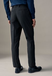 Pantaloni neri a taglio dritto, realizzati in tessuto liscio, con tasche laterali e tasche posteriori con bottone. Abbinati a scarpe nere.