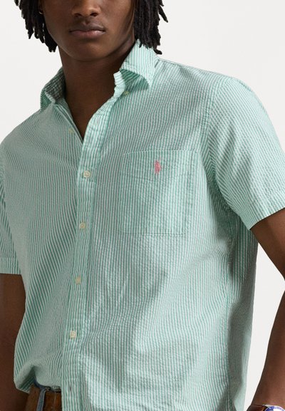 Camicia a maniche corte a righe verdi e bianche con colletto button-down, taschino sul lato sinistro del petto e un piccolo logo rosa sulla tasca. Vestibilità casual.