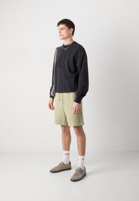 Czarna bluza z logo "HUGO", zestawiona z jasnoszarymi szortami z pasującym logo. Szare buty i białe skarpetki z czerwonym napisem dopełniają stylizację.